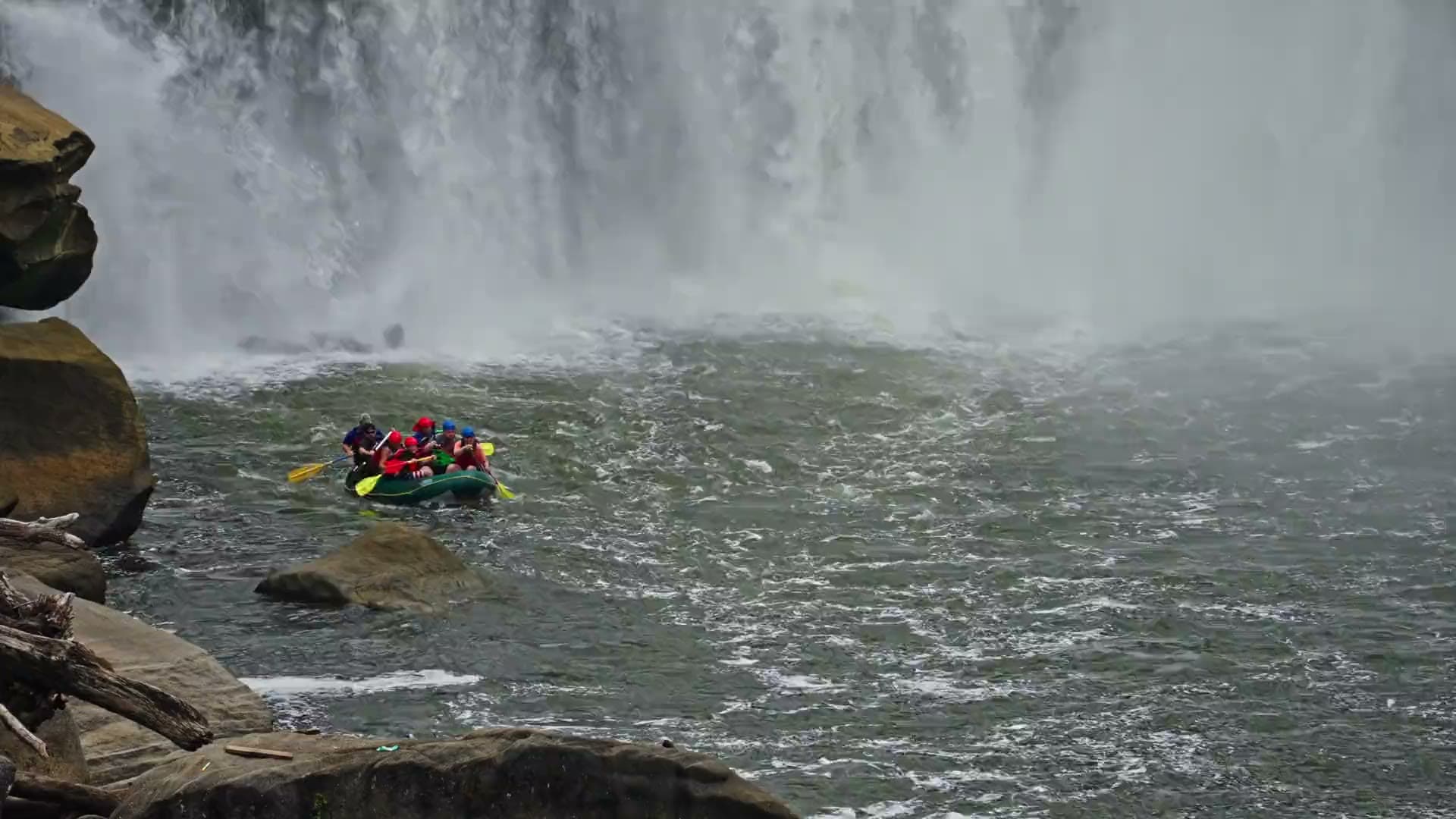 A raft of guests paddling through whitewater beneath the falls