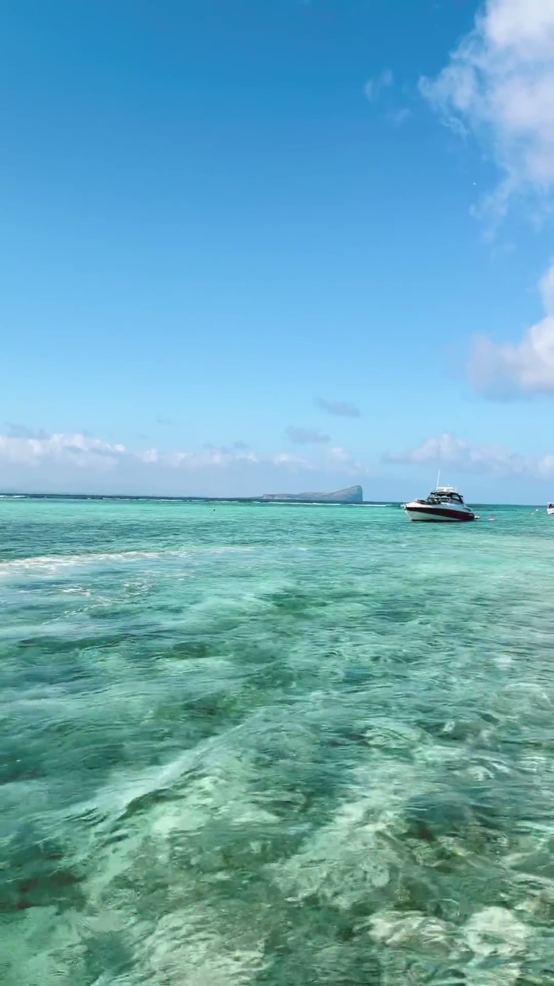 A boat anchored in turquoise shallows off Mauritius' north coast, with Coin de Mire on the horizon