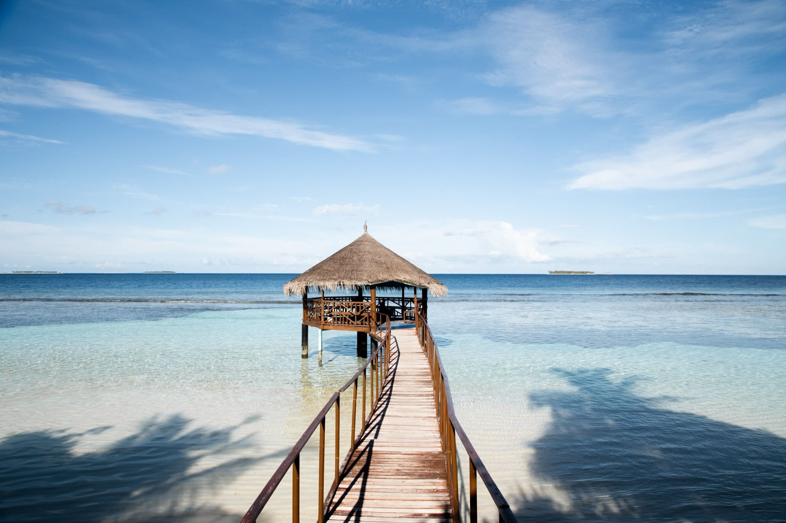 A thatched-roof jetty extending into a calm turquoise lagoon