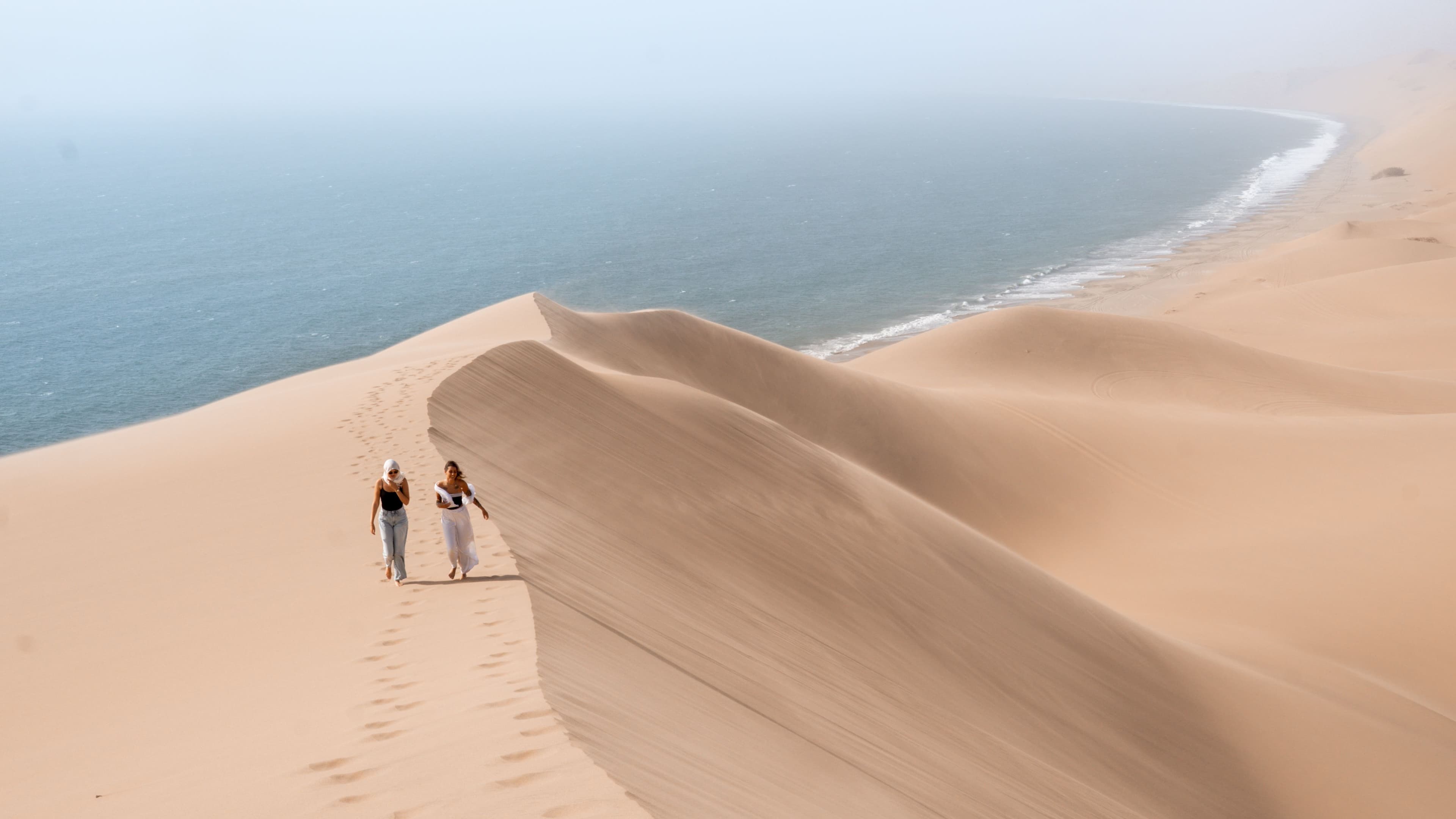 Walkers along a towering dune ridge above the cold Atlantic surf