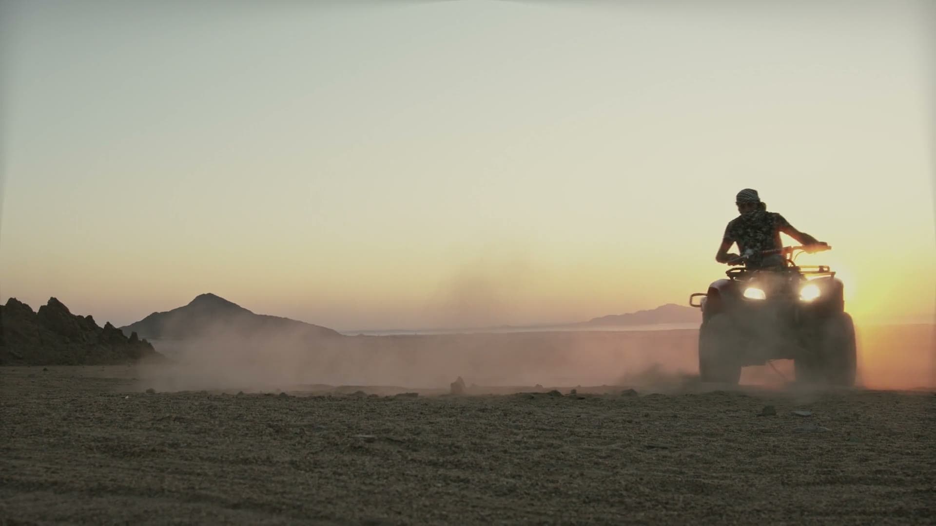 A quad bike kicking up dust across the dunes at sunset