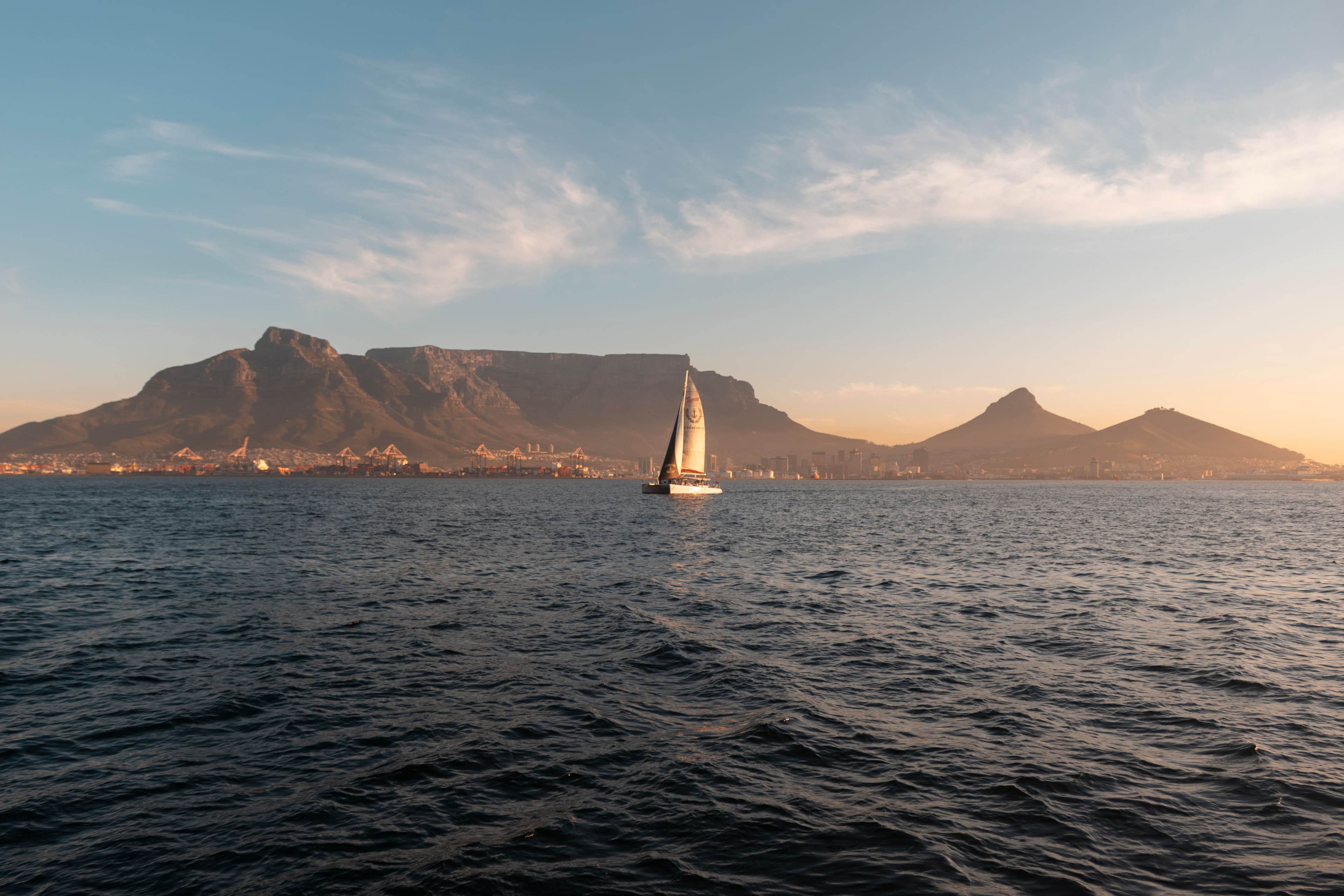 A sailboat crossing Table Bay at sunset with Table Mountain and Lion's Head behind