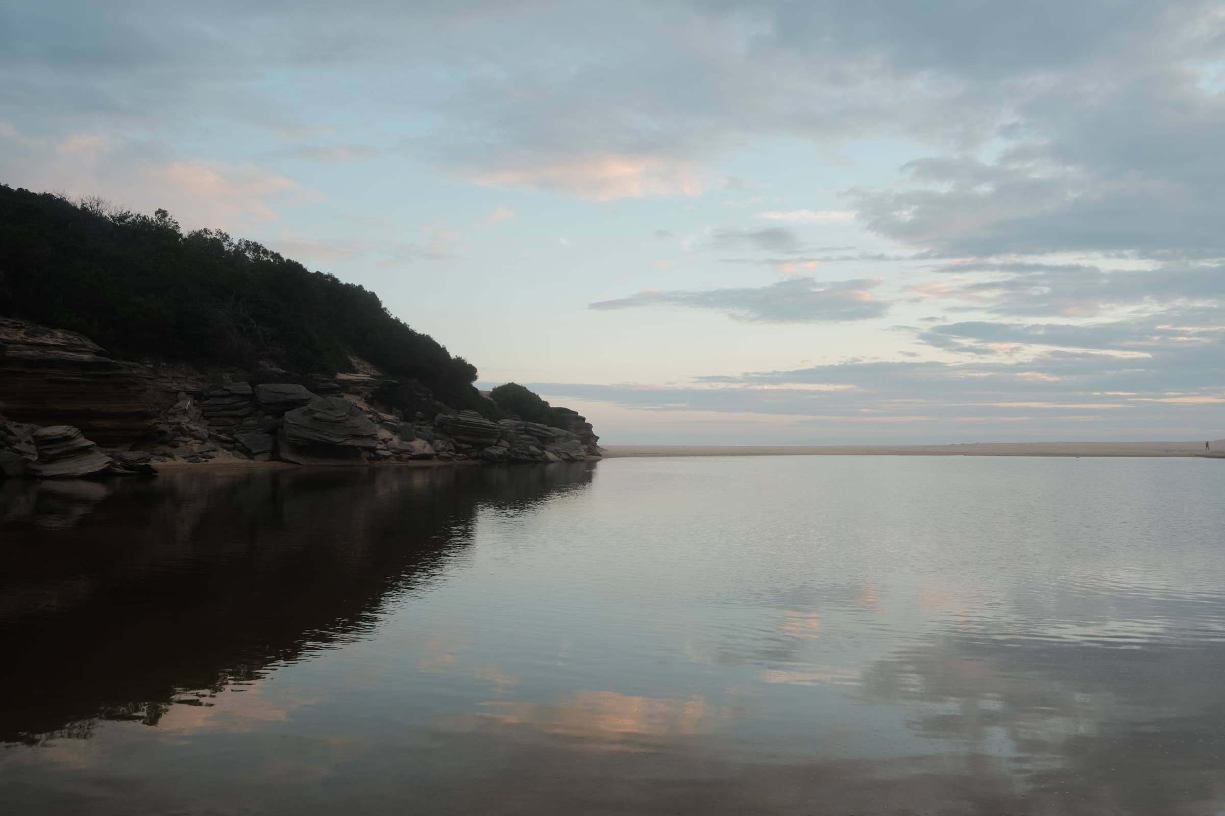 Layered sandstone cliffs meeting a calm lagoon at dusk