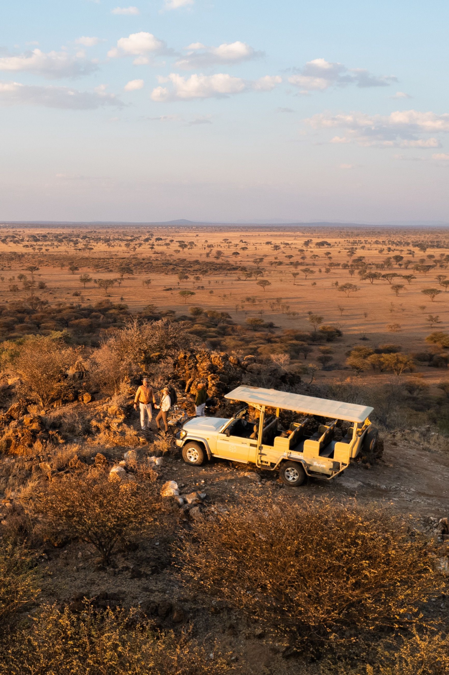 Safari vehicle and guests on a rocky escarpment overlooking the Rift Valley