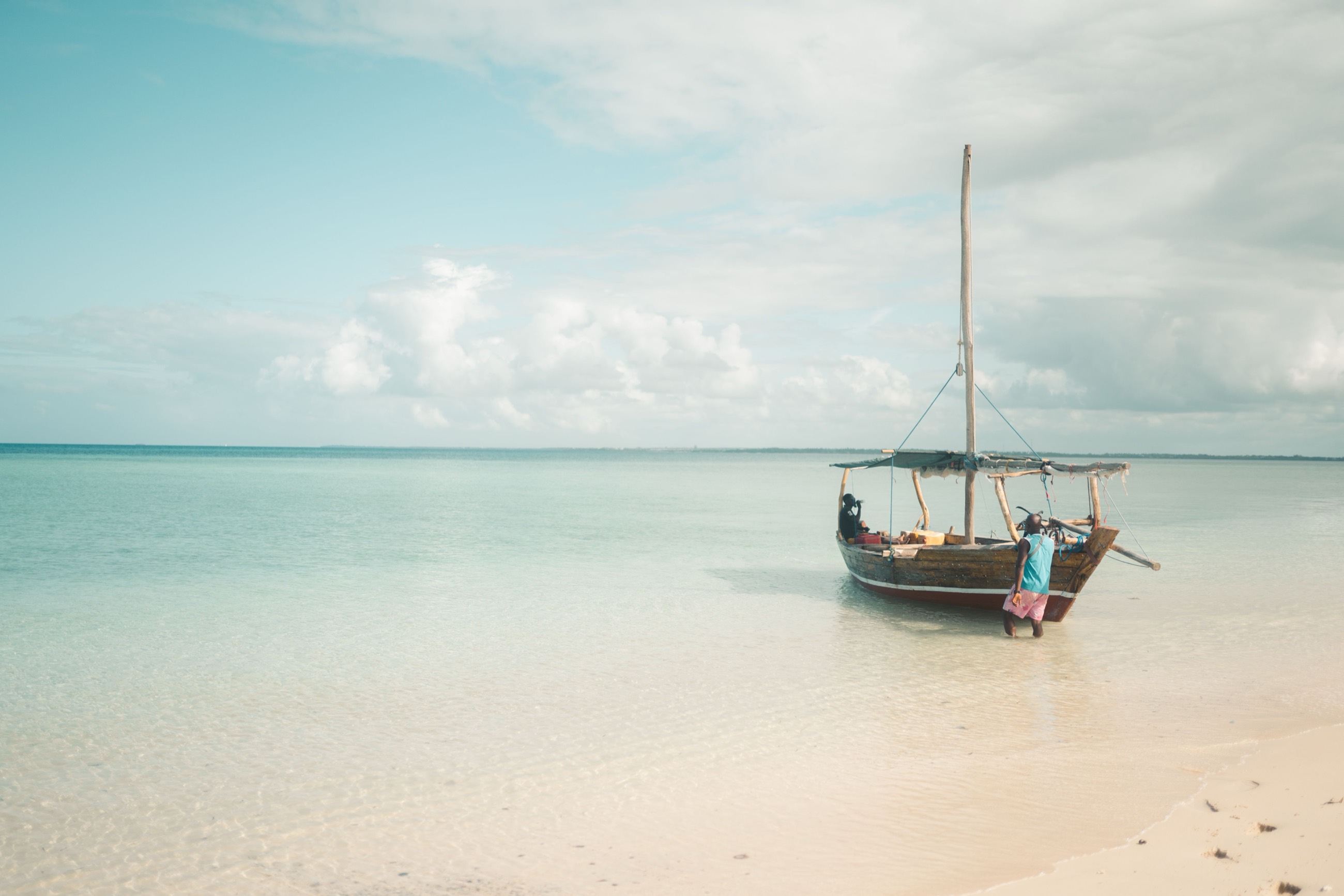 A dhow anchored in shallow water as guests wade out to board