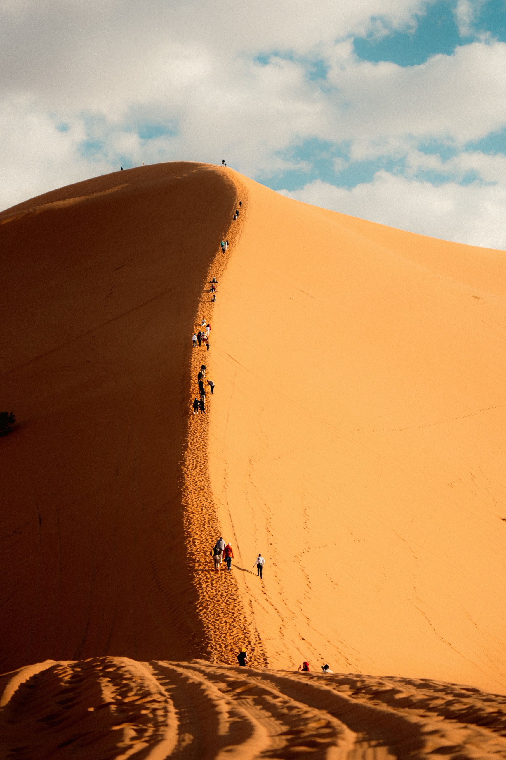 Hikers climbing the ridge of a giant dune at sunrise