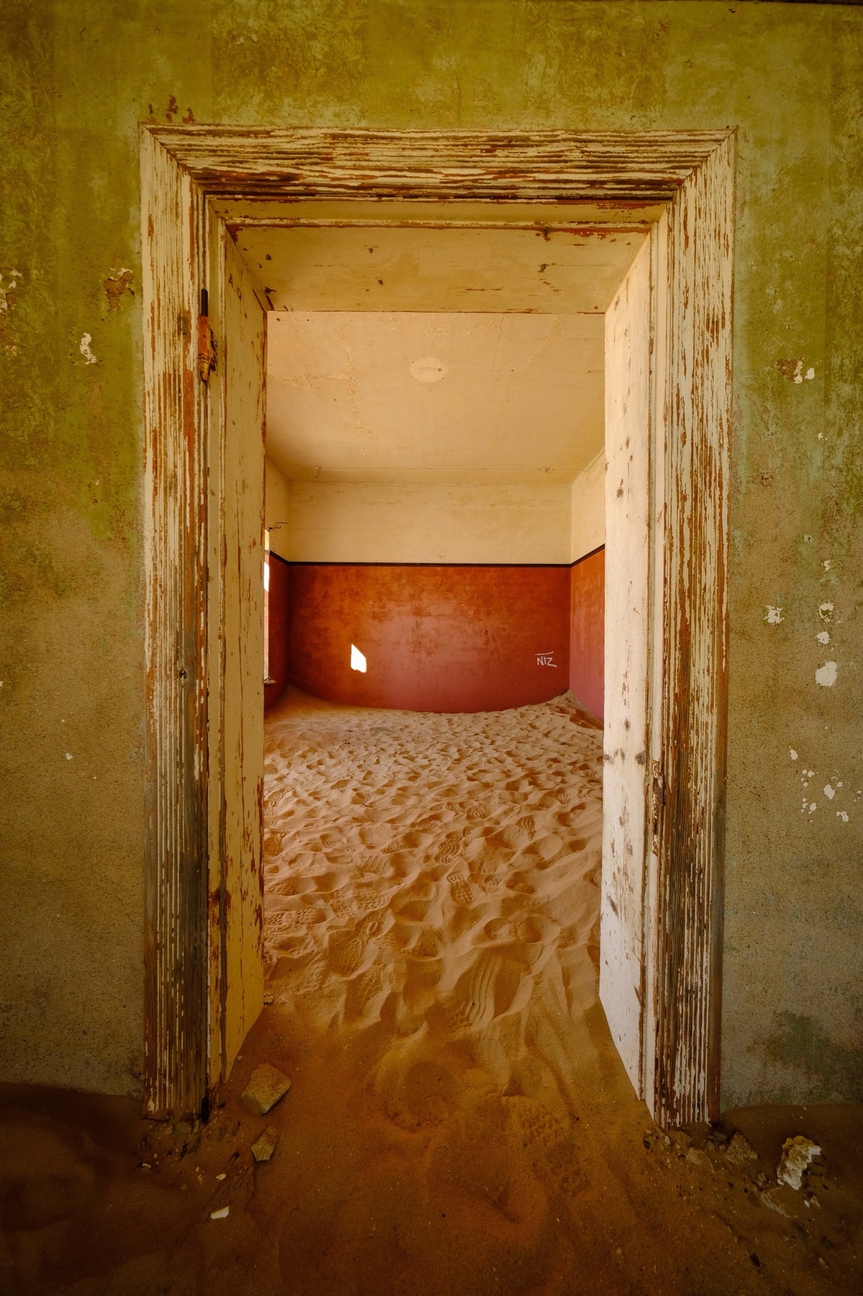 A sand-filled room with faded red walls at Kolmanskop