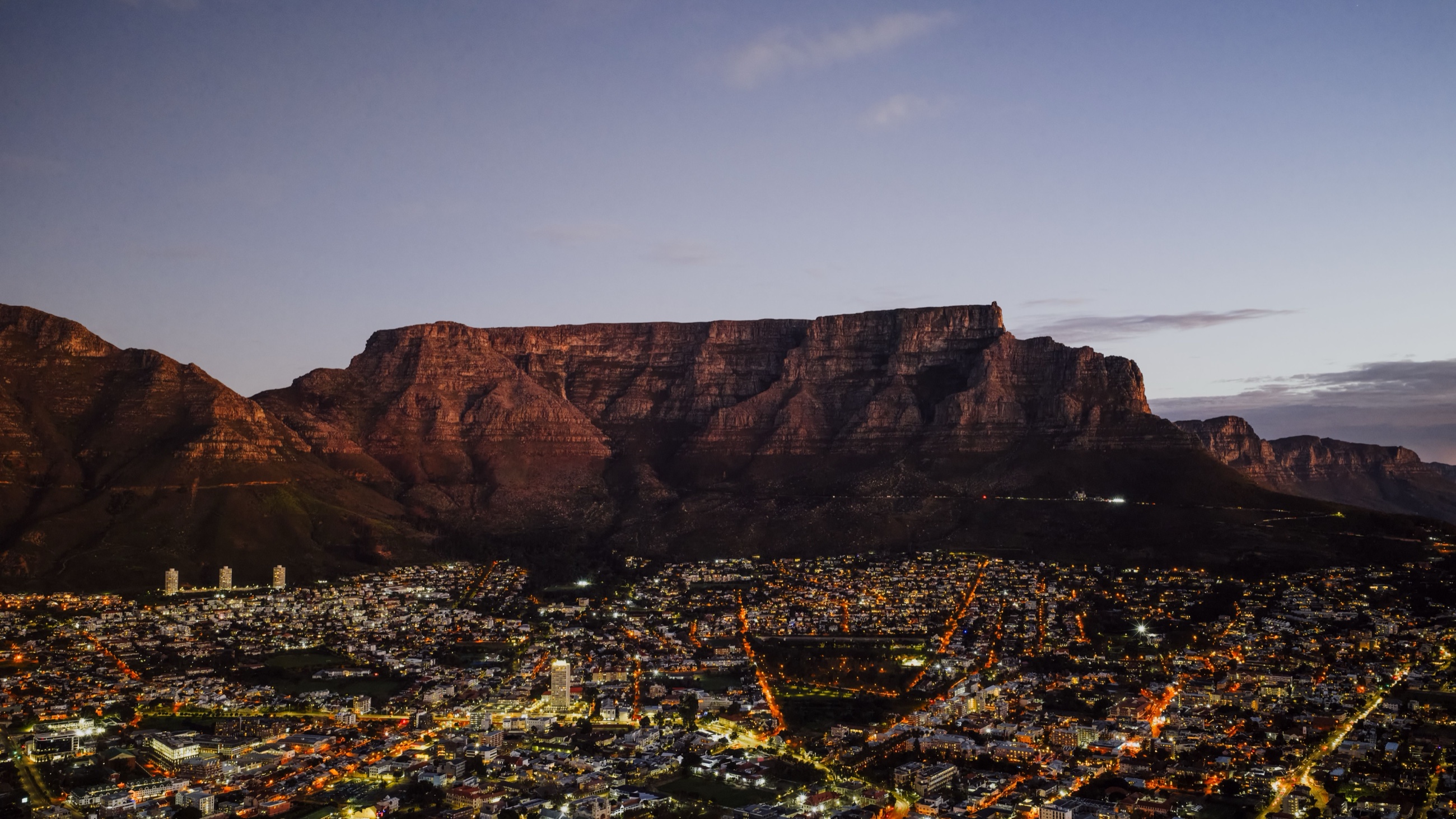 Table Mountain rising over Cape Town's city lights at dusk